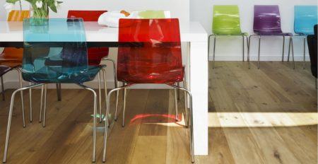 Colourful plastic chairs at white dining table opposite modern artworks on wall